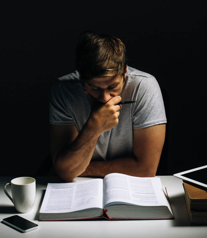 Young male sitting in dark and reading literature