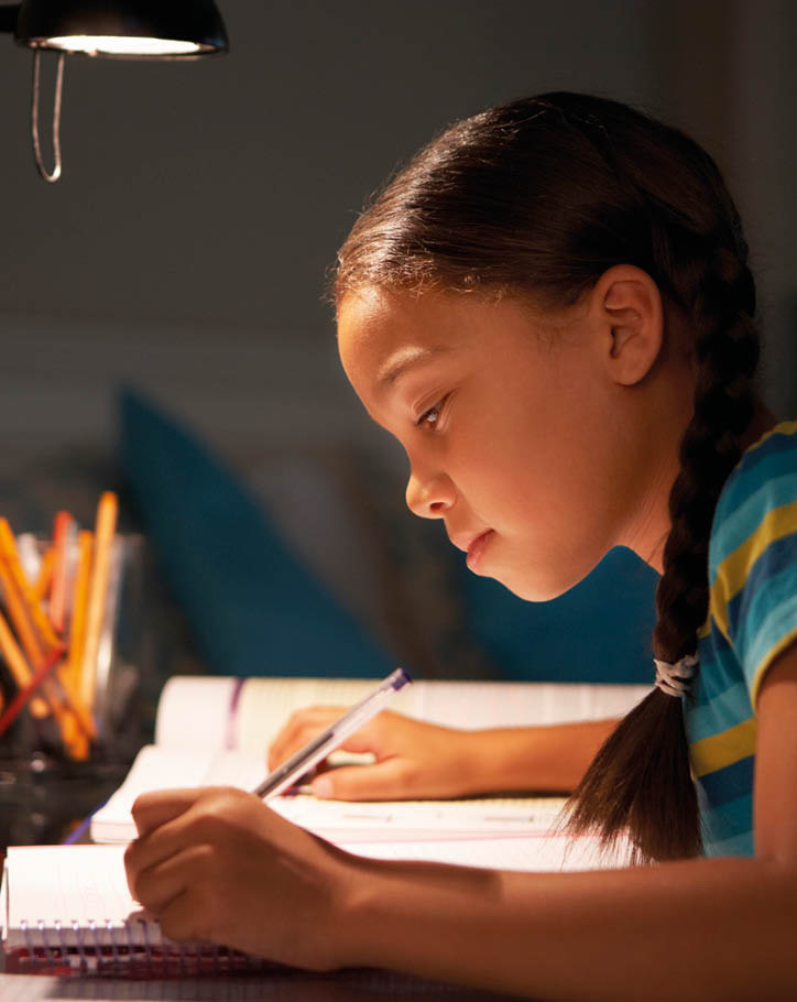 Young Girl Studying At Desk In Bedroom In Evening Writing Notes 