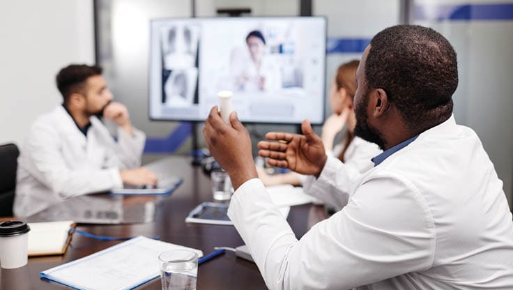 Young African-American healthcare worker talking to female colleague on computer screen during presentation at digital meeting