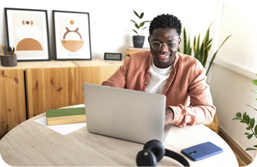 Happy black male university student studying at home using laptop. Education and technology