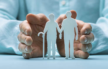 Hand Protecting Senior Couple Cutout Figures On Desk