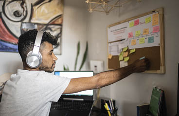 Young man sticking a note on the bulletin board at home