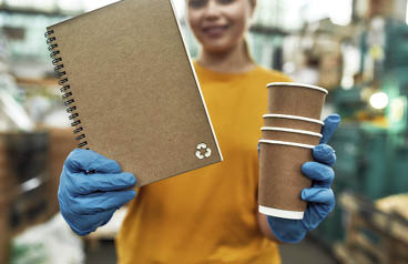 Selective focus on paper notebook produced from recycled cups held by girl working on waste station, cropped. Garbage sorting and recycling concept