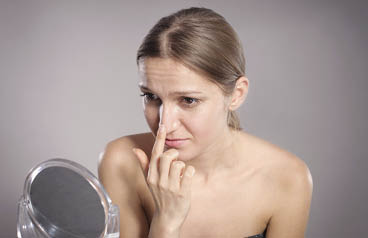 Young woman checks her nose in the mirror