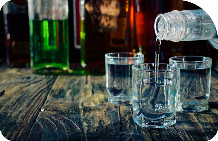 Pouring vodka into the shots on wooden bar counter. Close-up