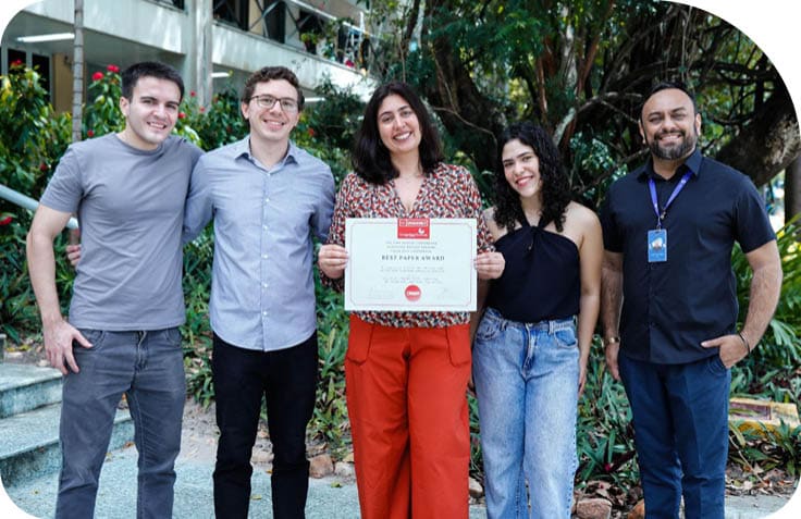 Cinco pessoas est o em p ao ar livre, uma delas segurando um certificado de premia  o, todas vestindo roupas casuais e sorrindo.  Description generated by AI