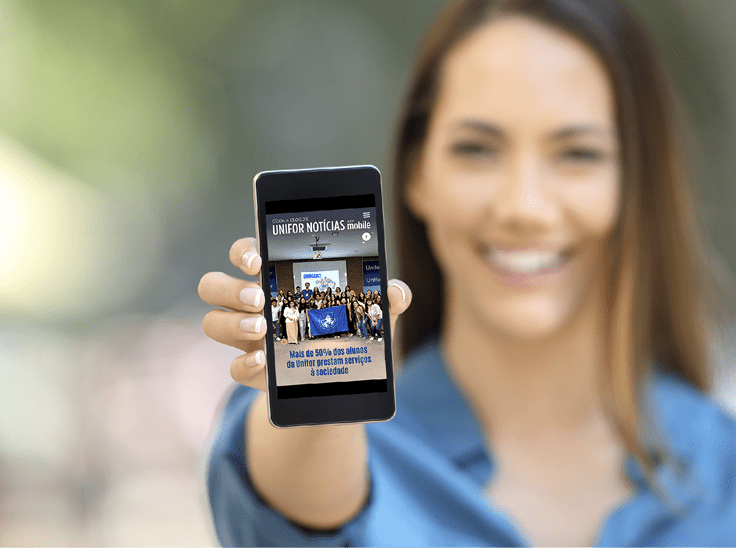 Pessoa vestindo camisa azul segura um celular que mostra a capa de uma revista digital intitulada Unifor Not cias com uma foto de grupo e texto em portugu s. Description generated by AI