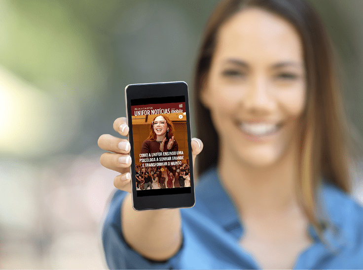 Pessoa sorridente segurando um celular com a capa de uma revista digital chamada Unifor Not cias exibida na tela. Description generated by AI