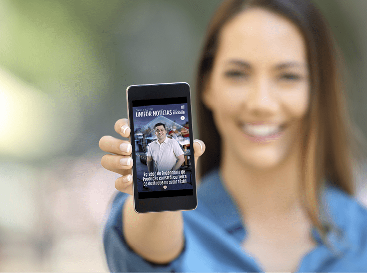 Pessoa sorridente com camisa azul segura um celular exibindo a capa de uma revista digital chamada UNIFOR NOT CIAS com a foto de uma pessoa e texto em portugu s. Description generated by AI
