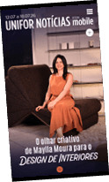 Pessoa com vestido laranja sentada em sof marrom em ambiente interno com prateleiras ao fundo em capa de revista sobre design de interiores.  Description generated by AI