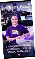 Pessoa sorridente com cabelo preso usando camiseta roxa com texto sobre marketing sentada em ambiente de escrit rio com notebook e caderno  frente.  Description generated by AI