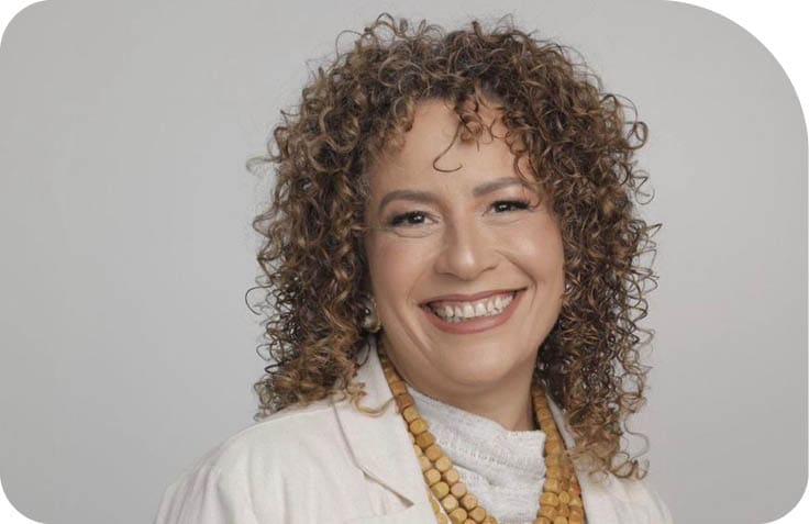 Pessoa adulta com cabelo cacheado sorrindo e vestindo roupa clara com colar de contas. Description generated by AI
