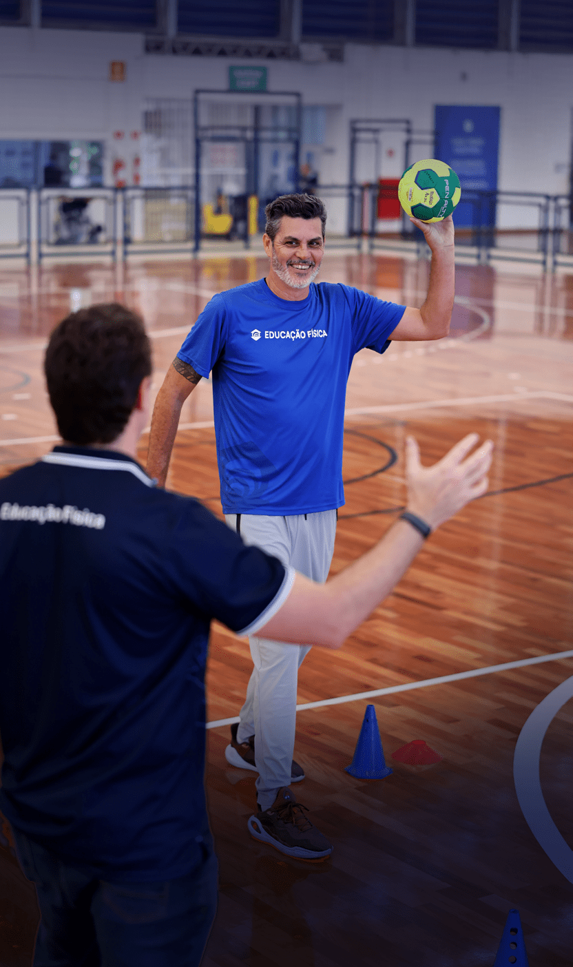 Duas pessoas em uma quadra esportiva interna, uma segurando uma bola colorida e sorrindo enquanto a outra est de costas com os bra os abertos.  Description generated by AI
