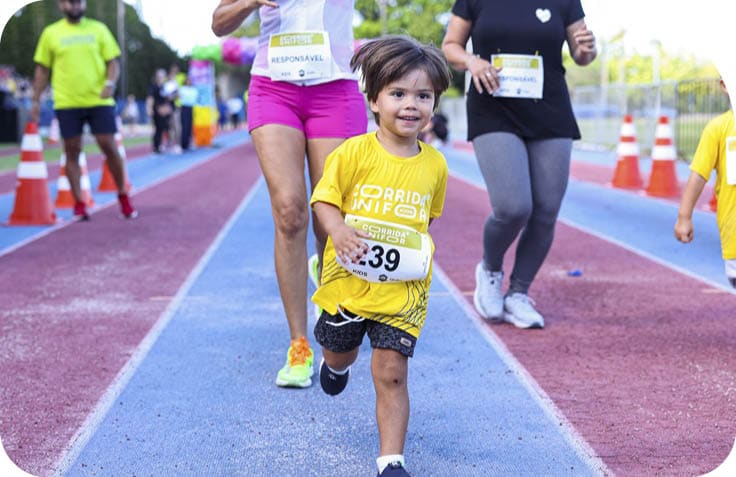 Crian a sorridente vestindo camiseta amarela corre em pista de corrida acompanhada por adultos tamb m com camisetas e n meros de competi o.  Description generated by AI