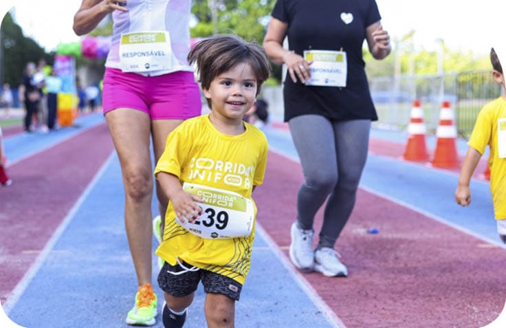 Crian a sorridente vestindo camiseta amarela e n mero de corrida participa de uma prova em pista ao ar livre acompanhada por adultos. Description generated by AI