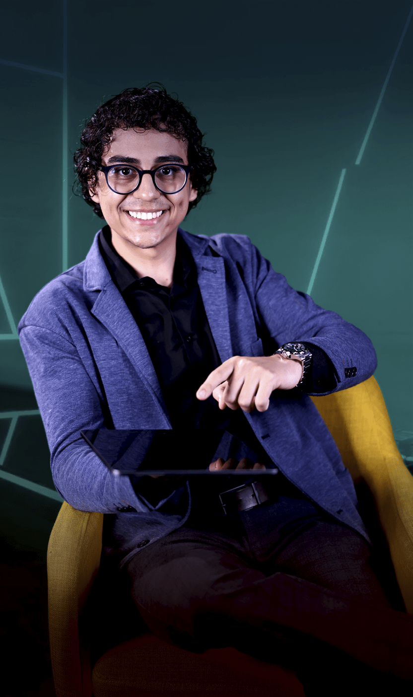 Pessoa adulta com cabelo cacheado e culos sorrindo enquanto aponta para um tablet preto sentado em uma poltrona amarela com fundo escuro.  Description generated by AI