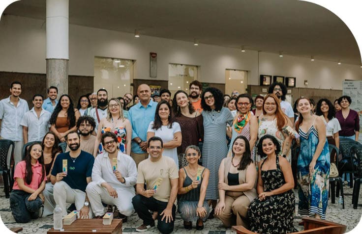 Grupo grande de pessoas sorrindo e posando para foto em ambiente interno com cadeiras ao redor. Description generated by AI
