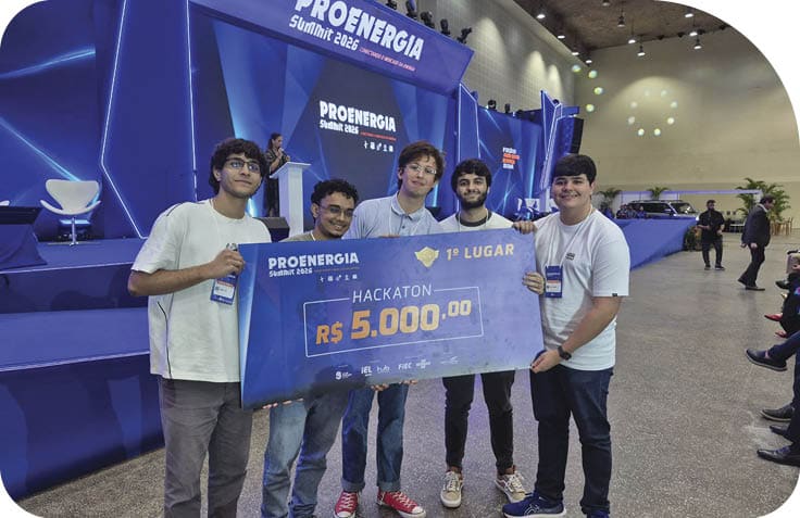 Cinco adultos jovens seguram um grande cheque simb lico de premia o em um evento de tecnologia chamado Proenergia Summit 2023 realizado em um audit rio com palco iluminado.  Description generated by AI