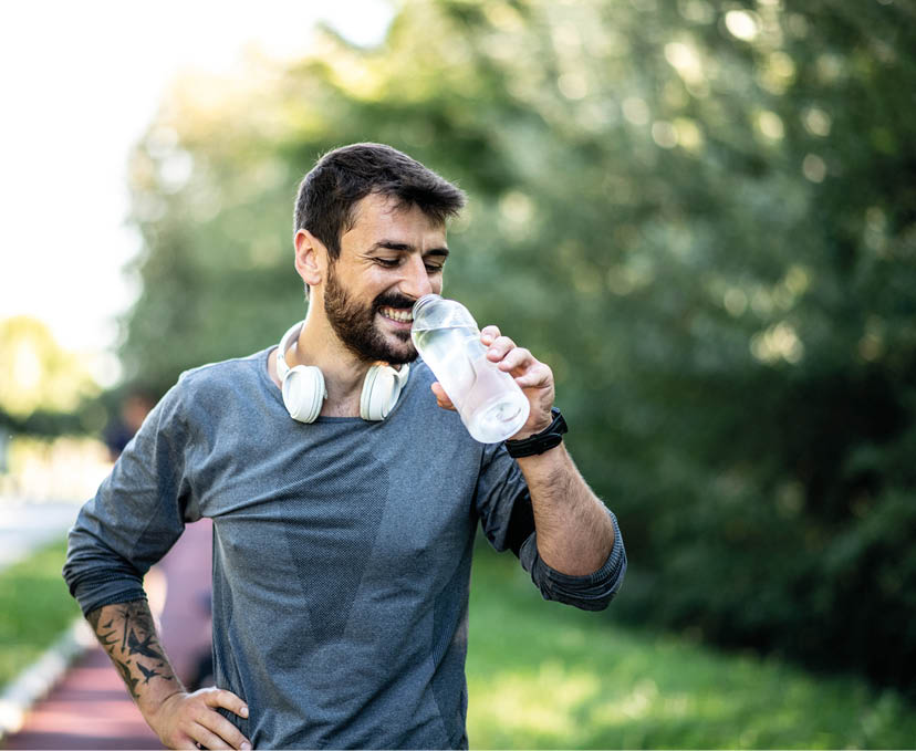 A young skinny Caucasian male is resting on a treadmill and drinking water