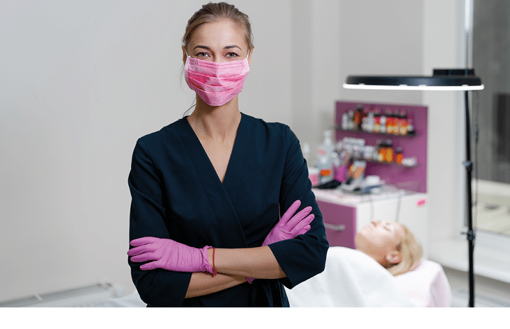 Cosmetology cabinet client lies on couch  Beautician stands in pink medical mask and smiles  Preparation for the procedure of permanent eyebrow makeup 