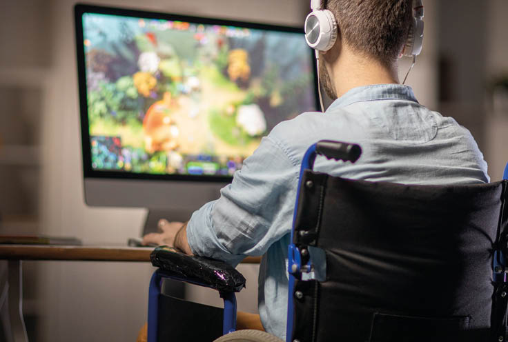 Rear view of editor or video designer in headphones sitting in wheelchair in front of computer screen and working with new content