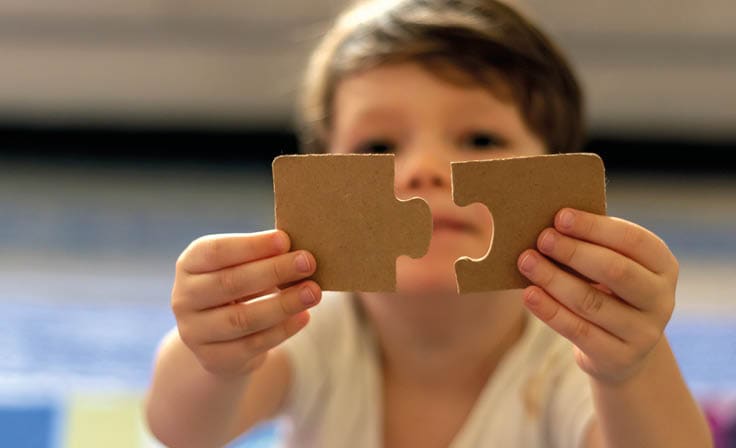 Puzzles in the hands of a child on colorful background Boy at home playing with puzzles Cute little child connecting a jigsaw pieces Portrait of toddler holding jigsaw puzzle block,looking at camera 